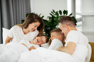 Obraz na płótnie Canvas Young family enjoying in bed. Happy parents with sons relaxing in bed..