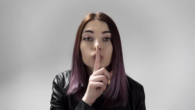 Portrait of young caucasian woman keeping a secret or asking for silence on the white background. Pretty lady brings forefinger to her lips. She makes shush movement. Theme of gesturing and signs.