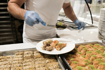 Staff in gloves serving Turkish baklava for tourists at all-inclusive hotel in Turkey. Delicious traditional sweets on a plate. Assortment of eastern treats for lunch at a luxury resort in Antalya.