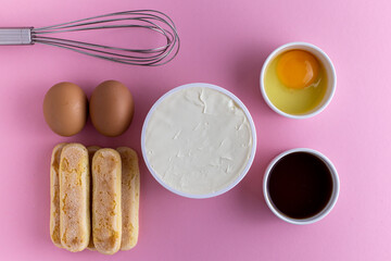 Ingredients for tiramisu, preparing tiramisu. Eggs, ladies finger cookies, mascarpone, coffee, whisk for beating eggs on a pink background.
