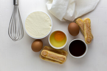Ingredients for tiramisu, preparing tiramisu. Eggs, ladies finger cookies, mascarpone, coffee, whisk for beating eggs on a white background.