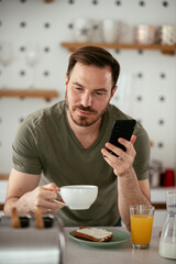 Young man eating breakfast and reading the news online. Handsome man enjoying at home