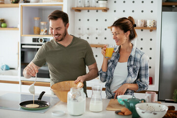 Husband and wife making pancakes at home. Loving couple having fun while cooking.