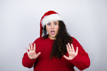 Young beautiful woman wearing a Santa hat over white background afraid and terrified with fear expression stop gesture with hands, shouting in shock. Panic concept.