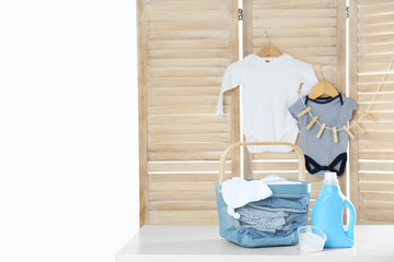 Basket with baby laundry, bottle of detergent and washing powder on white table