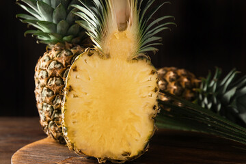 Whole and cut pineapples on wooden board, closeup