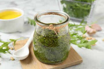 Jar of tasty arugula pesto and ingredients on white table