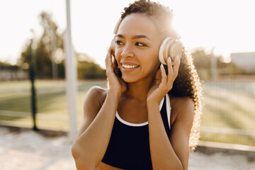 Athletic young african american woman listening to music in headphones, in sportswear outdoors in the park, healthy lifestyle and sport concept