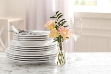 Set with clean dishes and vase of flowers on white marble table