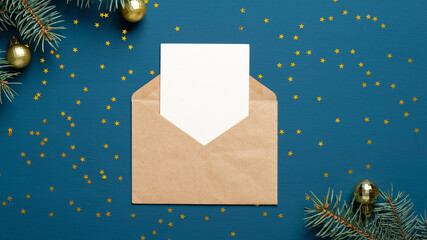 Craft paper envelope letter with blank white card mockup on dark blue background with golden confetti stars, fir branches, Christmas decorations. Christmas letter concept.