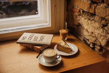 Obraz premium BUDAPEST, HUNGARY - Nov 03, 2019: Cup of coffee next to a piece of cake put on the windowsill