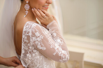 On the wedding day, a bridesmaid helps the bride to put on her wedding dress.