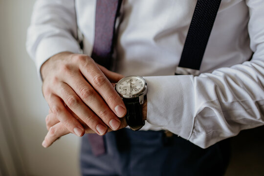 A business businessman in classic clothes looks at watch, controlling the time. Suspenders and a white shirt are part of the style. A man checks the time so as not to be late for a business meeting