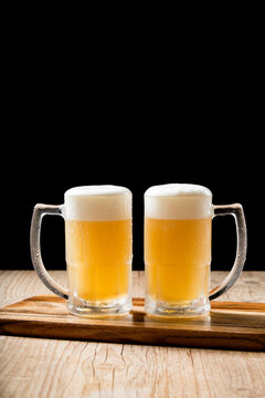 Two draft mugs beer on woden table and black background