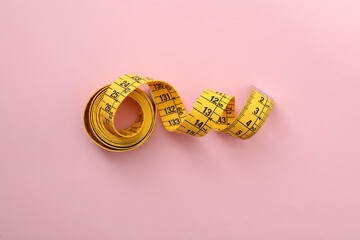 Yellow measuring tape on pink background, top view