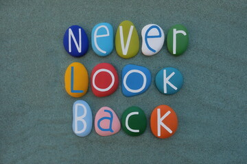 Never Look Back, motivational slogan composed with multicolored stone letters over green sand