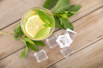 Looking down on a glass of iced lemon mint water and fresh mint leaves and scattered ice cubes on the table