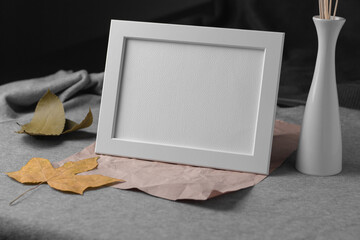 Empty white picture frame with leaves and vase