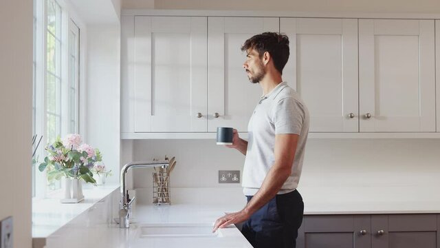 Morning shot of man standing by kitchen window relaxing with hot drink - shot in slow motion