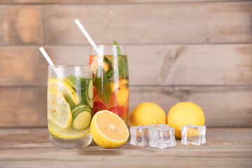Two glasses of iced lemon mint tea and fresh lemon fruit and ice cubes in summer