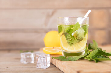Iced lemon mint water on the cutting board and fresh lemon fruit, ice cubes and fresh mint leaves next to the glass