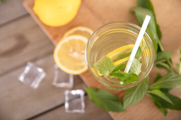 Iced lemon mint water on the cutting board and fresh lemon fruit, ice cubes and fresh mint leaves next to the glass