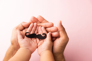 Fototapeta premium Father and his son kid uses hand holding black mustache, studio shot isolated on white background, Prostate cancer awareness month, Fathers day, minimal November moustache concept