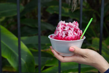 Ice desserts with topping red Syrup and sweet milk in women hand holding in nature