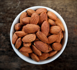 Almonds in white bowl on wooden table. Top view