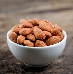 Almonds in white bowl on wooden table.