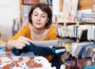 Young woman looking for interesting cloth in textile shop..