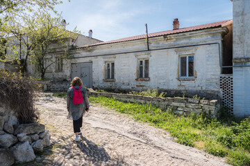 Fototapeta na wymiar A woman with a backpack on the street with a dirt road and houses built in the 19th century in the city of Kerch in the Crimea