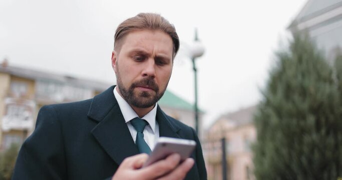 Portrait of bearded businessman in formal outfit using modern smartphone for work outdoors. Concept of business, success and technology.