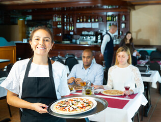 Portrait of smiling waitress with serving tray pizza at a restaurant