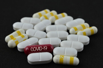 View of a red pill word - COVID-19 with many white and yellow pills, close up with blurred background. Medical concept of Virus Pandemic Protection, Coronavirus COVID-19.