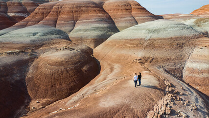 Couple looking out into a desert landscape resembling planet Mars. Rock layers with orange, red, blue, purple, and orange hues in the sediment can be seen 