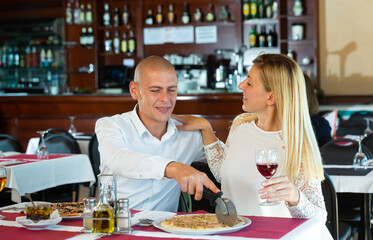 Fototapeta na wymiar Happy couple enjoying tasty pizza during romantic dinner with wine on date in cozy restaurant