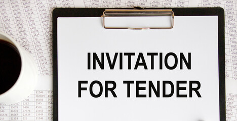 Text on the tablet with a pinned white sheet INVITATION FOR TENDER, a number of reports and coffee.