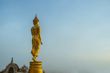 Big golden buddha in a standing position with blue sky background at Wat Phrathat Khao Noi in Nan Province, north of Thailand. 