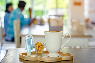 Mini portable alcohol gel bottle to kill Corona Virus(Covid-19) and biscuits and coffee cup on table with blurred image of a family eating at restaurant in background. Health care concept.