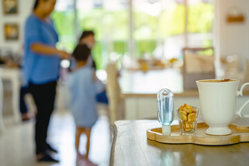 Mini portable alcohol gel bottle to kill Corona Virus(Covid-19) and biscuits and coffee cup on table with blurred image of a family eating at restaurant in background. Health care concept.