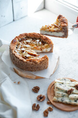 pie with dor blue cheese, pears and almond, whole round on a plate on a white table. Sugarless. Close up. Selective focus.