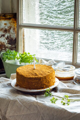 Homemade birthday cake with candle, honey cake. On a rustic table near the window. Food content.