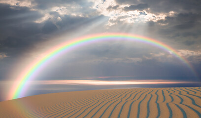 Rainbow over the sand dunes in the desert, calm sea in the background