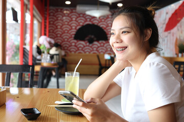 Asian women are smiling with holding the smartphone in restaurant.