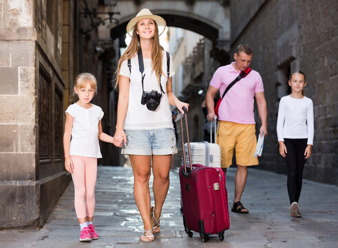 Happy russian traveling family of four strolling with luggage along European city street .