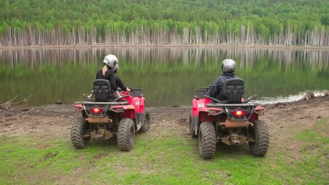 Tracking of people on red quad bikes driving and stopping by pond in forest, then taking off their helmets. They are chatting and enjoying scenery