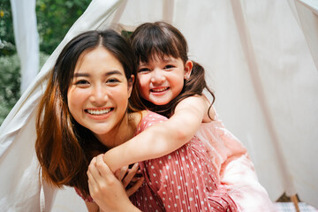 Asian mother and daughter piggy back outdoors at yard.