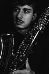 Grayscale shot of a handsome guy holding his saxophone on a dark background