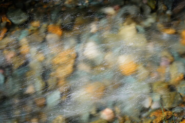 Rocky bottom of mountain river through the clear water, selective focus, blurring the image. Cristal water in the stream shimmers in sunlight. Stone background.